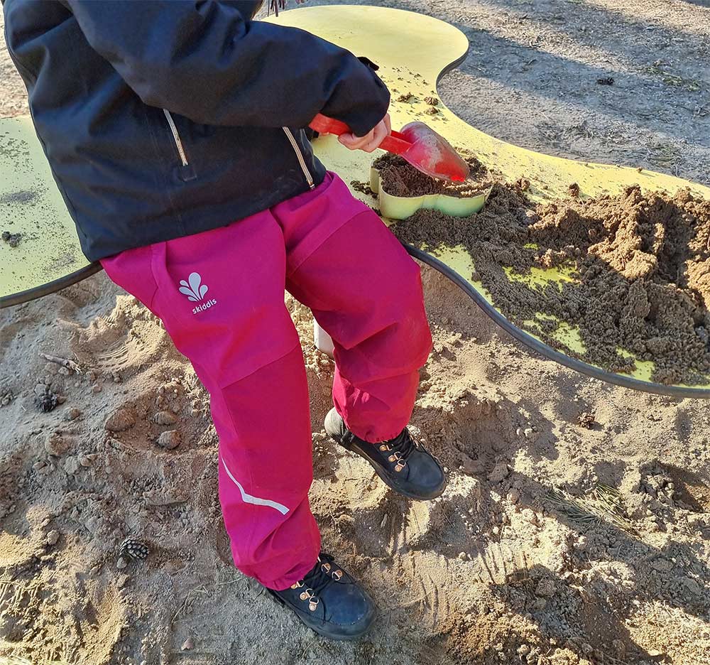 Enfant qui joue avec le sable au parc de jeux en pantalon de pluie pour enfant Skiddis